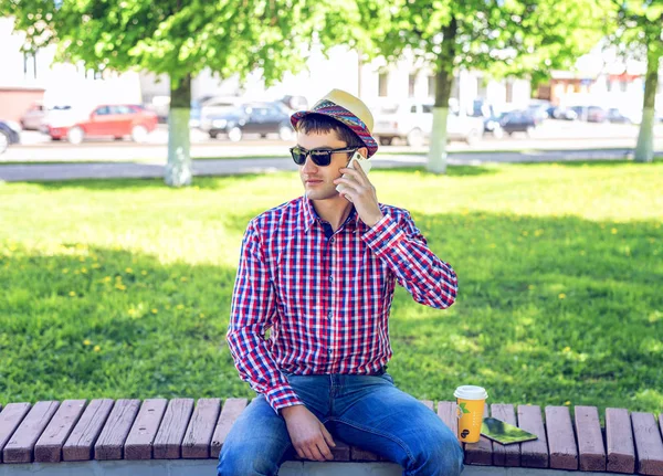 Mann sitzt bei Kaffee oder Tee, telefoniert, im Sommer in Brille und Hemd mit Hut im Wald, im Freien ruht ein Geschäftsmann und telefoniert mit dem Smartphone. — Stockfoto