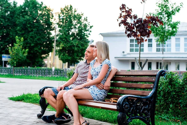 Joven pareja moderna sentada en el banco en el parque abrazando, en verano en la ciudad, horizontal, familia en la naturaleza está descansando, concepto de familia feliz, estilo de vida . — Foto de Stock