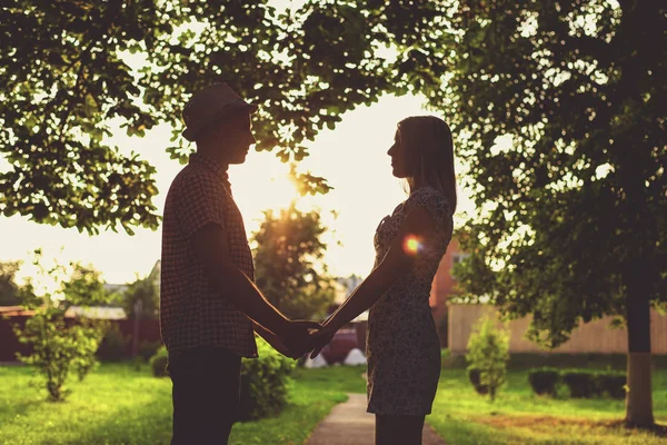 Ein Typ hält seine Freundin an der Hand, im Sommer in der Stadtsilhouette gegen den Sonnenuntergang, das Beziehungskonzept, das Brautpaar. Lifestyle ist der Sommer ein Kerl mit einem Mädchen. viel Laub in — Stockfoto