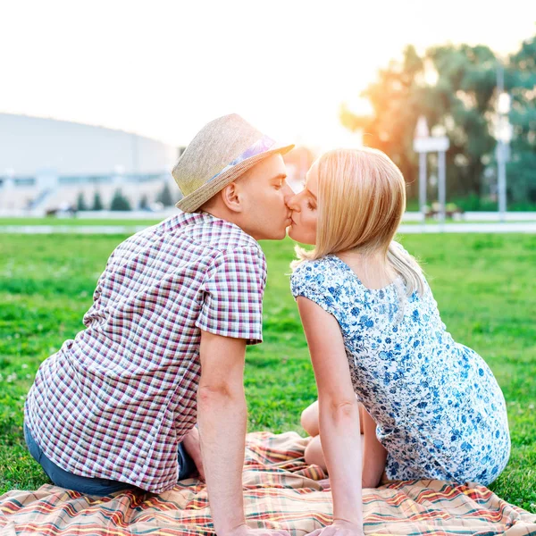 Fiatal modern pár a parkban, nyáron a város, vízszintes, család, a természet nyugvó, koncepció, boldog család, életmód. Nyilatkozat a szeretet. Csók a ül a takarón. — Stock Fotó