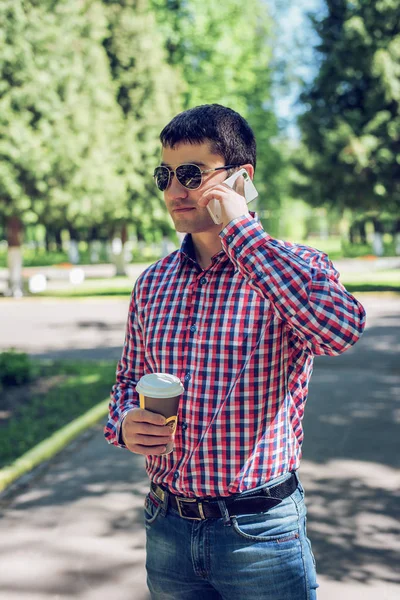 Mann in Hemd und Jeansbrille, telefonierend, Smartphone, Sommerkonzept, Geschäftsmann-Urlaub. Lebensstil in der Stadt. die Straße im Park. — Stockfoto