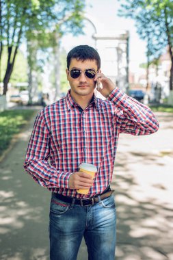 telefonu, akıllı telefon, yaz, işadamı tatil kavramı üzerinde konuşan adam bardaklarda, tişört ve kot pantolon. Şehir bir yaşam tarzı. Park Caddesi.