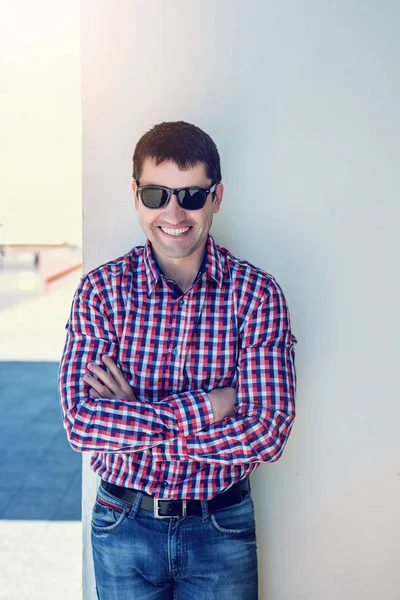 Der Mann im Sommer an der Wand, Brille, glückliches Lächeln, Jeans und Hemd, strahlend sonniger Tag. Die Idee des Konzeptunternehmers in der Stadt. Lifestyle, Porträt erfolgreich cl — Stockfoto