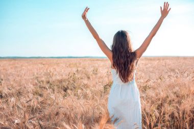 Bir kız yaz buğday alanında, ellerini beyaz elbisesini tabaklanmış deri, mutlu tatil temiz havada yükseltir. Güneşli bir gün. Doğanın keyfini. Seçim özgürlüğü.