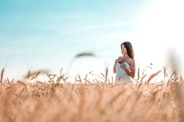Vackra lycklig kvinna i ett fält, solig eftermiddag, vit klänning. Vackert hår, solbränd hud, begreppet njuter av naturen. Vila på luften. Harmoni med vete. Blå himmel. — Stockfoto
