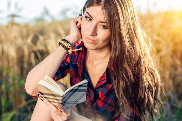 Beautiful happy brunette girl field is falling asleep, shirt. Concept new ideas, writing in notebook. Thinks on nature. A student reads a diary of a note. — Stock Photo, Image