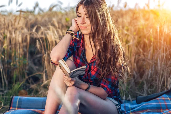 Schöne brünette Mädchen im Feld, Shorts. Konzept neuer Ideen, glücklich im frischen Sommer in der Natur. In seiner Hand ein Notizbuch, lange Haare. Notizen im Tagebuch studieren. — Stockfoto