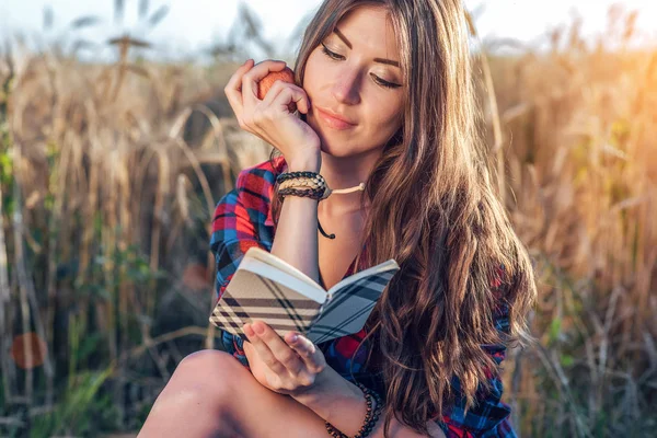 Hermoso campo de estudiante chica. En su mano manzana. Concepto de nuevas ideas, al aire libre, el verano en la naturaleza. En cuaderno de mano, pelo largo. Ideas inteligentes. Inspiración por la creatividad. Lee el diario . —  Fotos de Stock