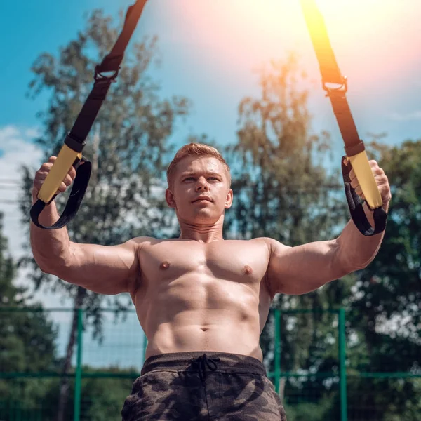 A male athlete is engaged in open air loops, trains the biceps. In summer, in shorts and a bare torso. Healthy lifestyle of young people. The concept of sport motivation. Close-up.