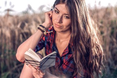 Buğday doğa, güzel esmer saçları rahatlatıcı bir alan gömlekli oturan kız. Bir not defteri fikrinin okur. Bir öğrenci okuldan sonra. Kavram notlar.