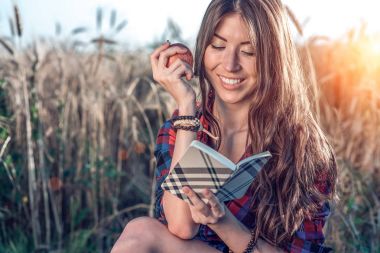 Buğday doğa, güzel esmer saçları rahatlatıcı bir alan gömlekli oturan kız. Bir elma, not defteri pnany gelecek için tutar. Mutlu gülümseyerek. Kavram notları görüşme için derslerdir.