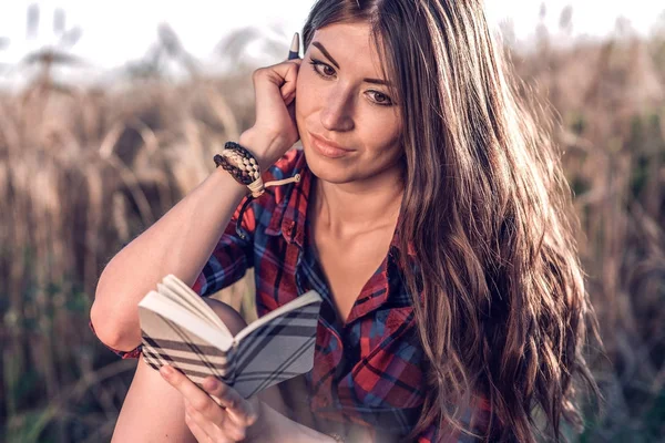 Buğday doğa, güzel esmer saçları rahatlatıcı bir alan gömlekli oturan kız. Bir not defteri fikrinin okur. Bir öğrenci okuldan sonra. Kavram notlar.