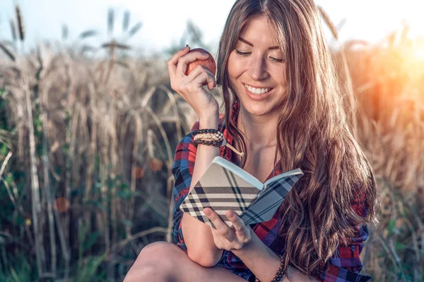 Buğday doğa, güzel esmer saçları rahatlatıcı bir alan gömlekli oturan kız. Bir elma, not defteri pnany gelecek için tutar. Mutlu gülümseyerek. Kavram notları görüşme için derslerdir.