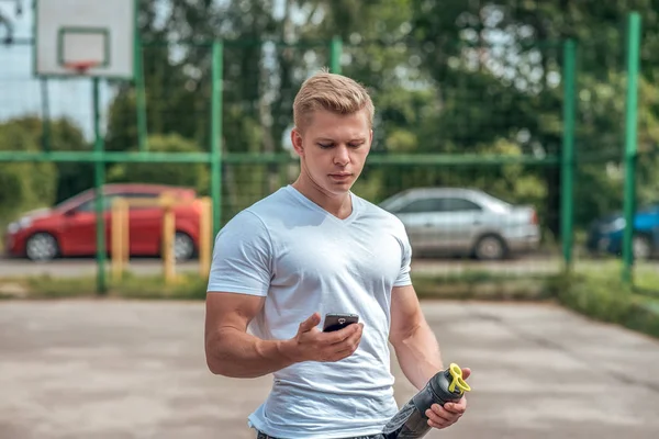 Adam telefon, sosyal ağlar, zaman ayarlı bir shaker, kasa, protein şişe el izliyor. Yaz şehirde. Kavram sağlıklı yaşam tarzı. Video izlerken smartphone. Otomobil park arka plan.