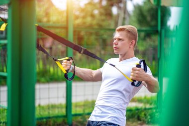 Atlet kol kasları pazı triceps kaslarının kayışlar. Bir adam bir atlet, menteşeleri üzerinde nişanlandı. Yeşil arka plan çit. At yere yaz. Temiz hava egzersiz. Sağlıklı yaşam kavramı.