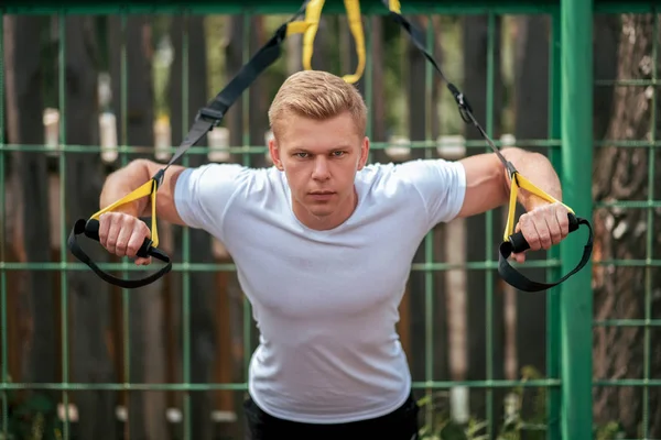 The athlete straps the muscles of the chest triceps. Male athlete, engaged in hinges, close-up. Have a fence in the summer. Exercise in the fresh air. The concept of a healthy lifestyle.