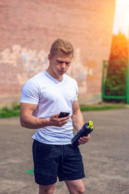 Bir adam telefonda, sosyal ağlar bir iletiyi okur, bir shaker, bir kasa, bir protein bir şişe verin. İçinde şehir yaz. Sağlıklı bir yaşam tarzı kavramı. Video izlerken smartphone.