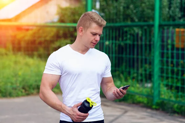 Der Mann beobachtet Timer am Telefon, soziale Netzwerke, die Hand eines Shakers, eine Flasche Tresor, ein Protein. in der Sommerstadt. das Konzept eines gesunden Lebensstils. im Smartphone Video ansehen. — Stockfoto