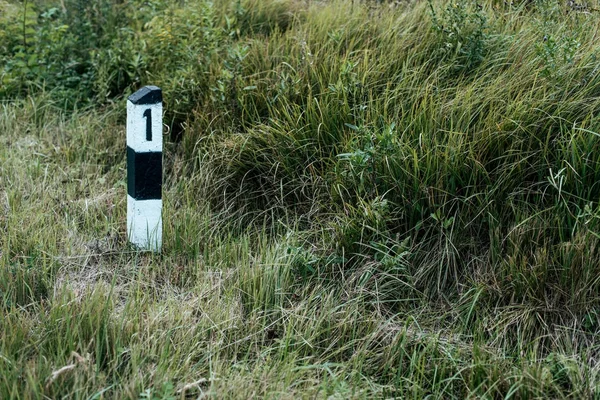 Betonnen pijler met nummer één, achtergrond groen gazon op de weg, concept van het begin van het pad. Het idee van de eerste weg in het leven. — Stockfoto