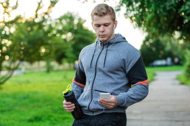 Smartphone, sosyal ağlar bir ileti yazar. Sporcu adam kulaklıklar müzik dinlemek. Bir shaker enerjik bir protein ile tutar. Telefonda uygulama ile eğitim. Yaz aylarında