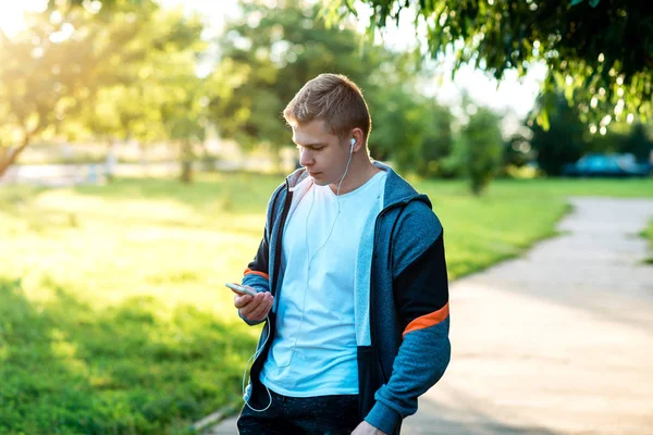 Ein Mann ist ein Sportler in der Natur, eine Straße in der Stadt und schreibt eine Nachricht in sozialen Netzwerken. im Sommer im Park. Lebensstil. Smartphone in der Hand, um Musik zu hören. — Stockfoto