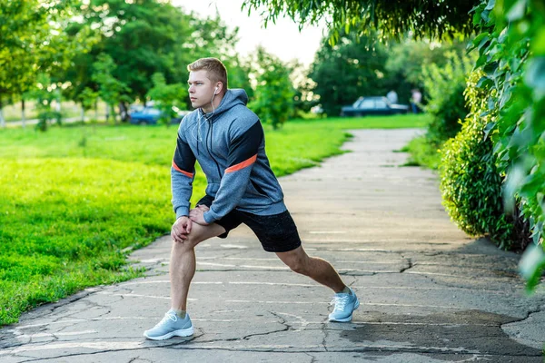 Чоловік-спортсмен прогрівається перед бігом у парку. Слухає музику на навушниках . — стокове фото