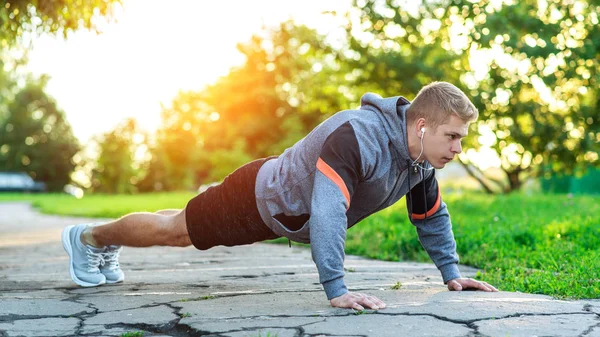Молодий атлетичний чоловік робить віджимання. М'язистий і сильний хлопець тренується. У природі в парку влітку. Сила та мотивація — стокове фото