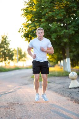 Bir erkek Koç kulaklık çalışıyor. Parkta koşucu sabah. Müzik, kendinden emin bir görünüm dinliyor. Yaz yaşam tarzı, motivasyon güçlüdür. Açık havada şehirde.