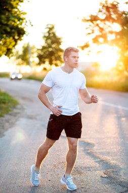Bir atlet olarak koşu bir beyaz T-shirt ve şort runner akşamları. Bir adam parkta bir audiobook, kendinden emin bir göz dinler. Yaz yaşam tarzı, motivasyon güçlüdür. Park açık havada.