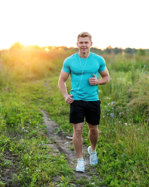 Athlete in a T-shirt and shorts runner in the evening, jogging. Happy smiling summer lifestyle, motivation strong. Outdoors in the park. A man in the park listens to an audiobook, a confident look.