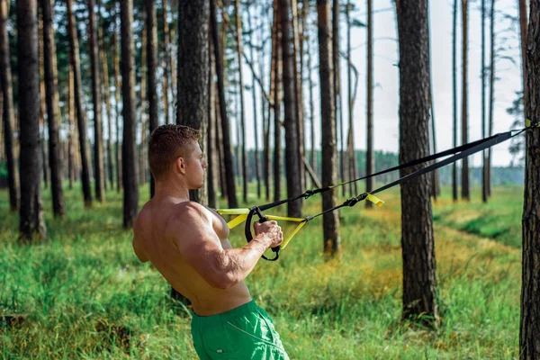 Чоловік-спортсмен займається петлями під відкритим небом, штовхаючи на паркан. Влітку, в шортах і білій футболці. Здоровий спосіб життя — стокове фото