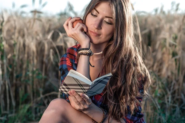 Beautiful girl student field. In his hand apple. Concept new ideas, outdoors, summer in nature. In hand notebook, long hair. Clever ideas. Inspiration by creativity. Reads the diary. — Stock Photo, Image