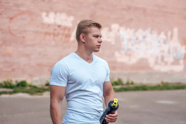 A male athlete goes in for sports in the open air. Muscular arms. Blonde in a white T-shirt. Lifestyle of the bodybuilder — Stock Photo, Image