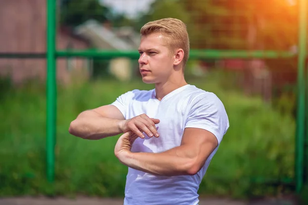 Ein männlicher Sportler treibt Sport an der frischen Luft. Muskulöse Arme. Blondine im weißen T-Shirt. Lebensstil des Bodybuilders — Stockfoto