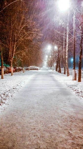 Ein nächtliches Unwetter im Winter in der Stadt, die Straße mit Schnee bedeckt. Schneegestöber fliegt neben Laternenmasten. — Stockfoto