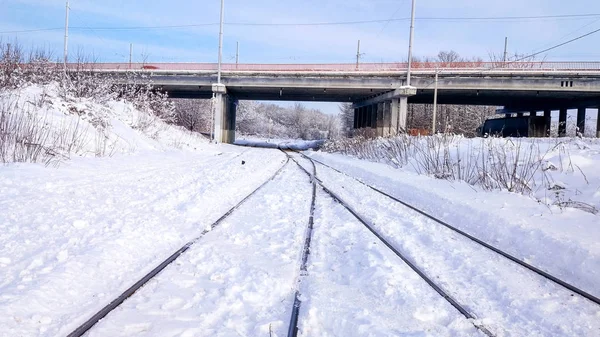 Sebuah jembatan mobil di seberang persimpangan kereta api. Tukang tidur dari kereta, kereta listrik di kota di musim dingin. Mereka diselimuti salju dari badai. Jalan menuju ke kejauhan . — Stok Foto