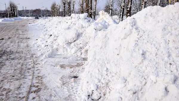 Pembersihan salju di musim dingin di kota. Tumpukan besar salju yang dikumpulkan oleh mobil di pinggir jalan. Dibersihkan aspal untuk mobil . — Stok Foto