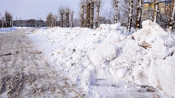 Pembersihan salju di musim dingin di kota. Tumpukan besar salju yang dikumpulkan oleh mobil di pinggir jalan. Dibersihkan aspal untuk mobil . — Stok Foto