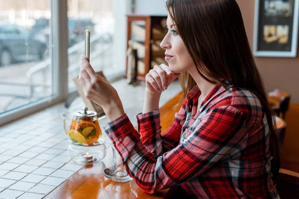 Kız öğrenci gömlekli, öğleden sonra pencerenin, kafede telefon görünüyor okur bir mesaj gülümseyen.