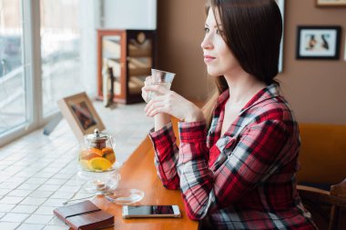 Bir kız öğrencinin gömlekli, gün boyu pencere, Düşler ve fantasies, tarafından bir kafede çay bir fincan ellerini, telefon ve bir çaydanlık yanında tutar.