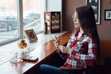 Bir gömlek gözlük, öğleden sonra bir kafede penceresinde elleri tarafından giyen bir kız öğrencinin cep telefonu tutan, posta görünüyor, sosyal ağlar denetler. Masada bir çay bardağına yoktur ve