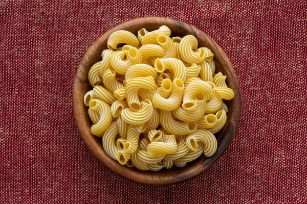 Pasta rigati en un tazón de madera sobre un fondo de arpillera de tela marrón roja en el centro . — Foto de Stock