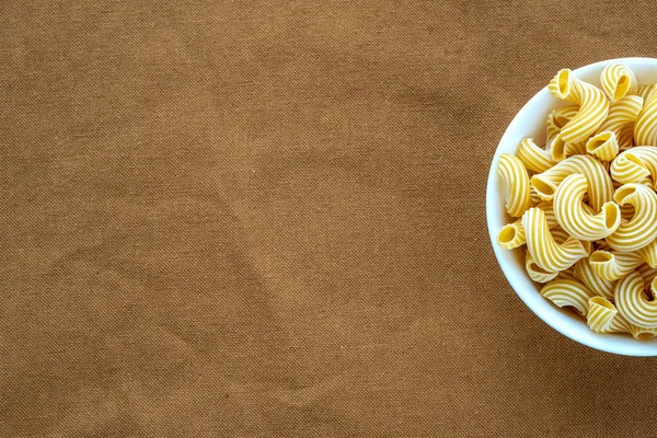 Pasta rigati en tazón blanco en patrón de arpillera de tela marrón beige con lado. Con espacio para texto . — Foto de Stock