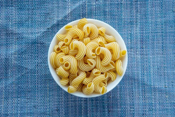 Rigati Pasta en una taza blanca sobre un fondo azul de punto en el centro . — Foto de Stock
