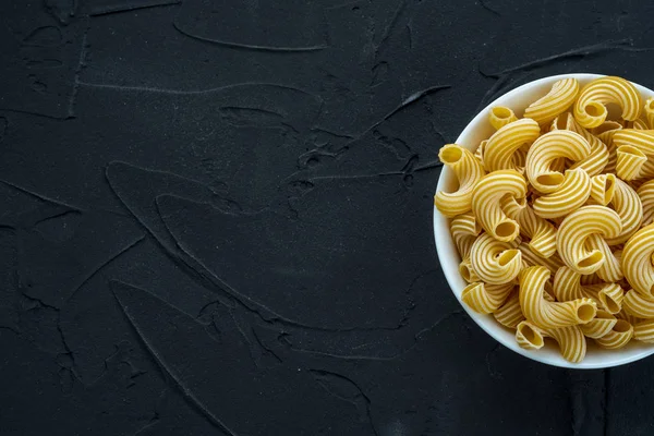 Rigati Pasta en un tazón blanco sobre un fondo negro texturizado por el lado. Con espacio para texto . — Foto de Stock