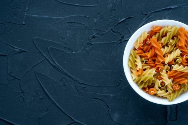 Çok renkli sarmal makarna makarna tarafından gelen siyah dokulu arka plan üzerinde beyaz bir kase. Top yakın çekim. Metin için ile yer.