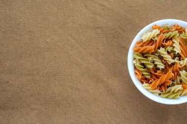 Çok renkli sarmal makarna makarna bir tarafı ile kahverengi rustik arka plan dokusu üzerinde beyaz bir kase. Top yakın çekim. Metin için ile yer.