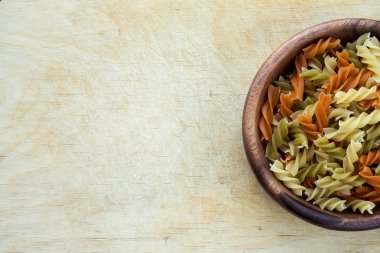 Çok renkli sarmal bir tarafı ahşap masa dokulu arka plan üzerinde ahşap bir kapta makarna makarna. Top yakın çekim. Metin için ile yer.