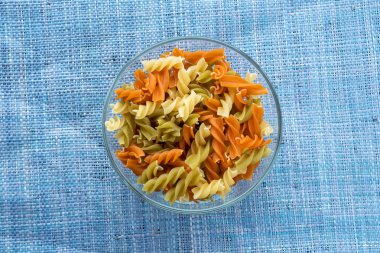 Çok renkli sarmal makarna makarna merkezinde mavi örme arka plan üzerinde bir cam kabın içinde. Top yakın çekim.