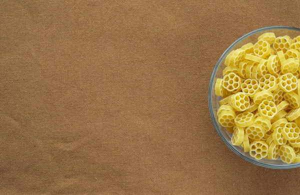 Macaroni ruote Pasta in a glass cup on a brown suburban background texture with a side. Close-up with the top. Free space for text. — Stock Photo, Image